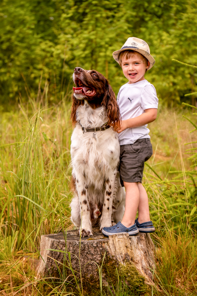 Kindershooting outdoor - Kind mit Hund steht auf einem Baumstamm